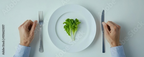 Hands poised over a plate with a single lettuce leaf on a white background. photo