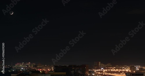 Time lapse of the moon moving across the sky over a city in the night lights. Aerial view