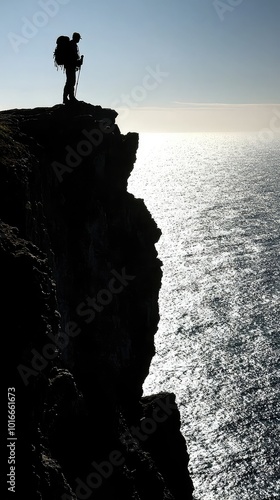 A silhouette of a hiker standing on a cliff, overlooking a serene ocean under a bright sky. A perfect moment of adventure. photo