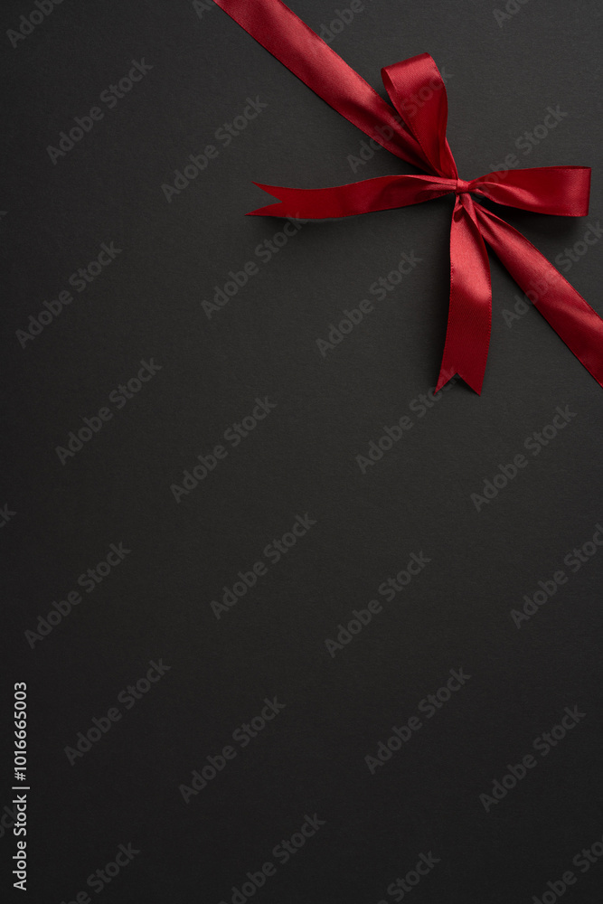 Fototapeta premium A stylish vertical red ribbon tied neatly into a bow against a dark backdrop. Perfect for themes of elegance, celebration, and gift wrapping