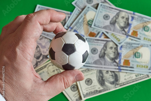 Cuadro en lienzo Soccer souvenir ball in hand against a background of hundred dollar bills, sport