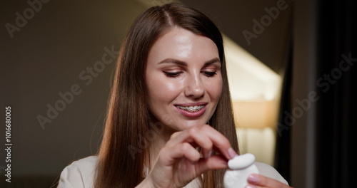 Smiling woman with dental braces cleaning teeth with dental floss at home. Close-up of young woman focusing on oral hygiene, ensuring braces stay clean and healthy. Orthodontic care and dental health.