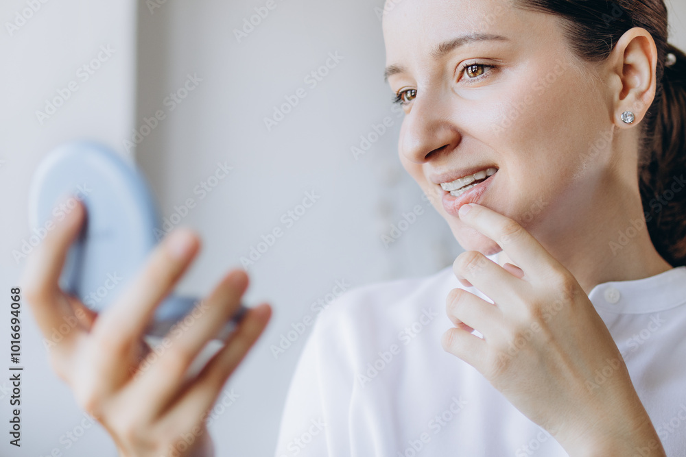 Young Woman Is Checking Her Teeth For Imperfections In A Small Mirror. New Technology For Teeth Straightening. Dental Health Medical Care Concept. Young Woman Is Checking Her Teeth For Imperfections In A Small Mirror. New Technology For Teeth Straightening. Dental Health Medical Care Concept.