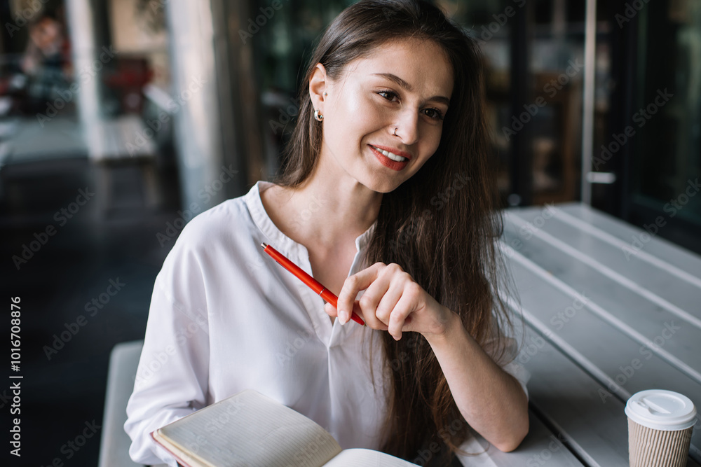 Smiling hipster girl dressed in casual wear feeling good during time for exam preparation sitting in coffee shop with knowledge notepad, happy intelligent female student enjoying planning project Smiling hipster girl dressed in casual wear feeling good during time for exam preparation sitting in coffee shop with knowledge notepad, happy intelligent female student enjoying planning project
