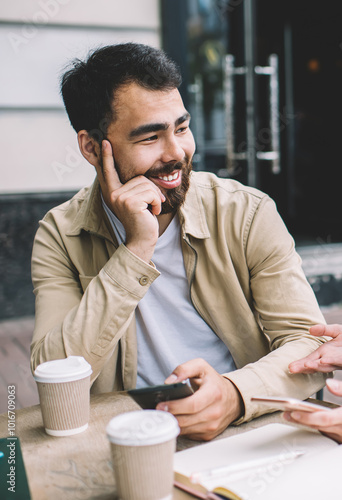 Cheerful male and female friends discussing new smartphone notification during knowledge time in street coffee shop, happy couple in love talking about ideas for joing blog in social networks photo