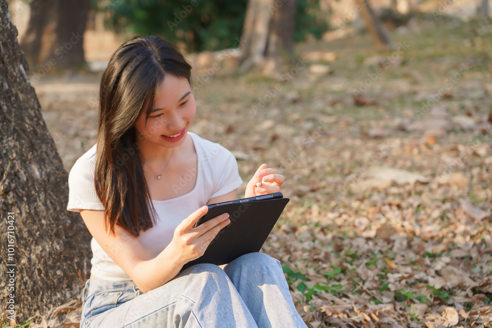 Young asian women sitting on the grass under tree in the nature park and using digital tablet to writing business information while working outside and relaxation with journey travel lifestyle Young asian women sitting on the grass under tree in the nature park and using digital tablet to writing business information while working outside and relaxation with journey travel lifestyle
