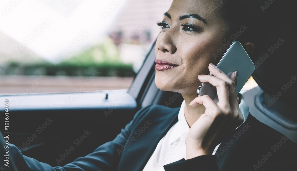 Fototapeta premium Professional female driver concentrated on road trip in automobile making international call conversation with colleague for discussing time of business meeting, woman trader using smartphone gadget