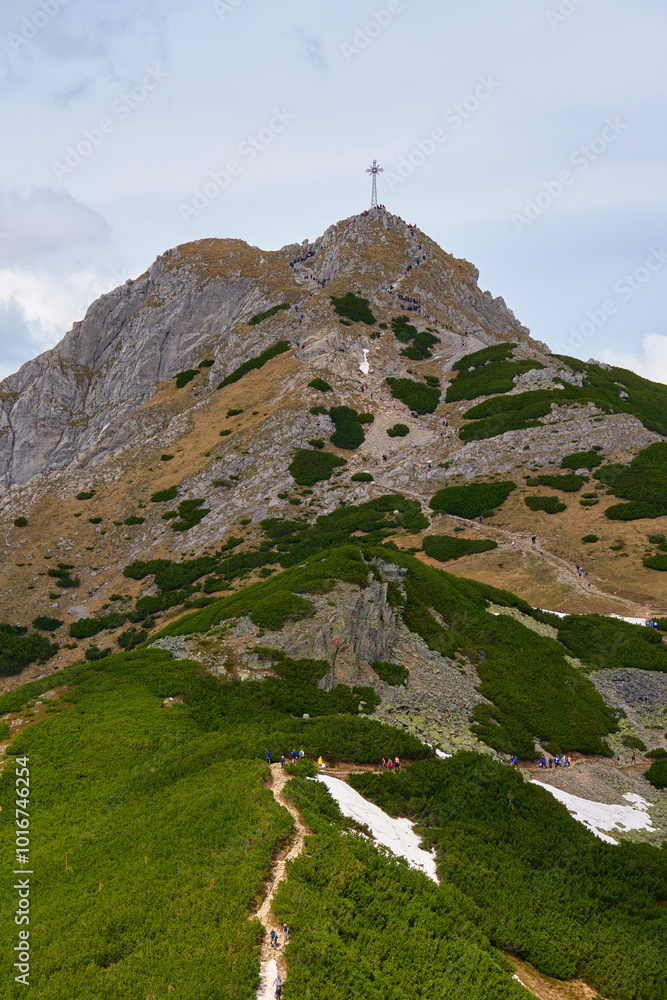 Fototapeta premium Rugged hiking trail leading to mountain summit with large cross under cloudy sky. Tatra mountains in Zakopane, Poland. Giewont mountain summit. Natural landscape
