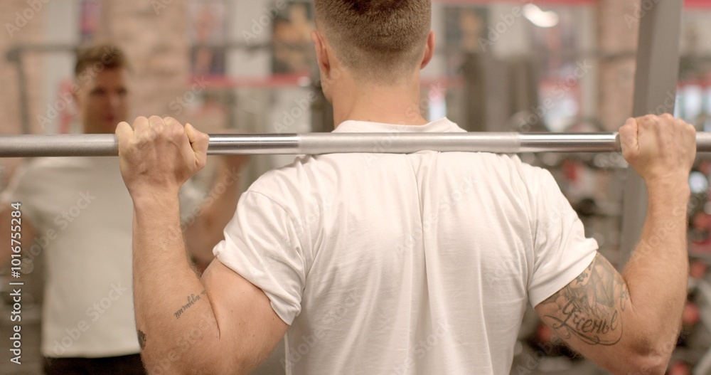 Fototapeta premium Back and leg workout with weighted squats man is seen from behind, lifting weights in a gym. Emphasis on fitness and strength training