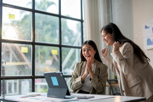 Two excited businesswomen celebrating success while looking at tablet in modern office