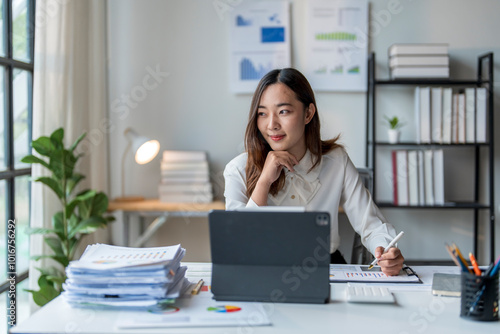 Young asian businesswoman thinking while working on tablet in modern office