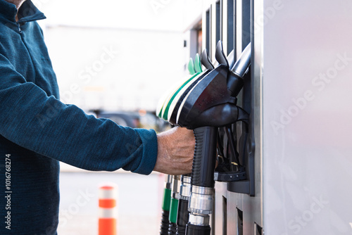 Man refueling transporter bus, taking a fuel nozzle out of holder or putting it back into a pistole holder. Vehicle gasoline refill process captured in action.