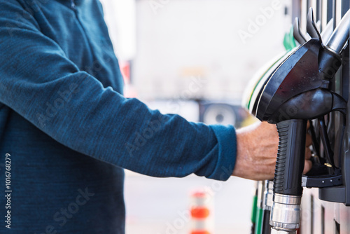 Man refueling transporter bus, taking a fuel nozzle out of holder or putting it back into a pistole holder. Vehicle gasoline refill process captured in action.