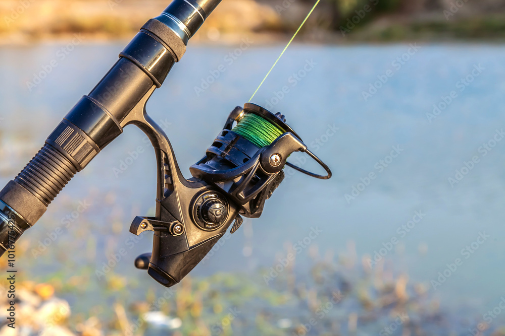 Spinning fishing reel. Fishing on the lake. Fishing rod against the background of the lake close-up. Fishing background. Spinning fishing reel. Fishing on the lake. Fishing rod against the background of the lake close-up. Fishing background.