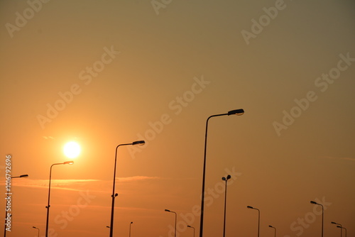 A sunset scene with a deep orange sky, where the sun is low on the horizon. Streetlights are silhouetted against the sky Outdoor nature landscape cityscape