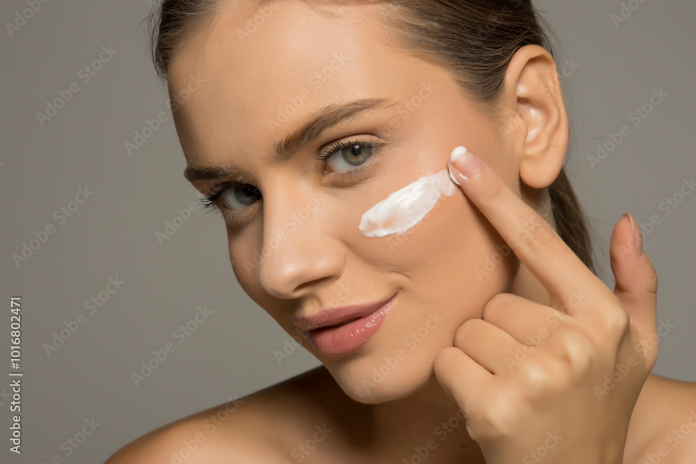 Beautiful young smiling woman applies a face cream on a gray studio background. Beautiful young smiling woman applies a face cream on a gray studio background.