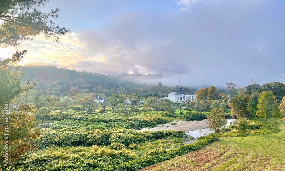 Naklejka premium Early morning panorama landscape scene of small town Vermont with a church, fall colors, and dramatic clouds
