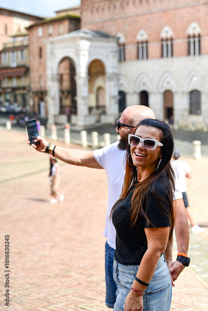 Fototapeta premium Happy smiling couple of tourists walking at Piazza del Campo at Siena. Concept of Italian gastronomy and travel. Italian couple having aperitivo together