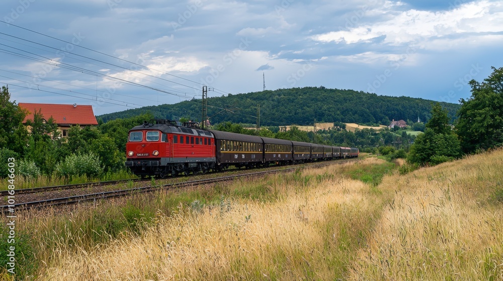 Bright red train travels through a lush countryside under a dramatic sky at dusk Bright red train travels through a lush countryside under a dramatic sky at dusk