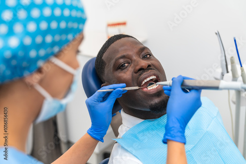 Dental hygienist using precision tools during an oral examination on an African male patient.