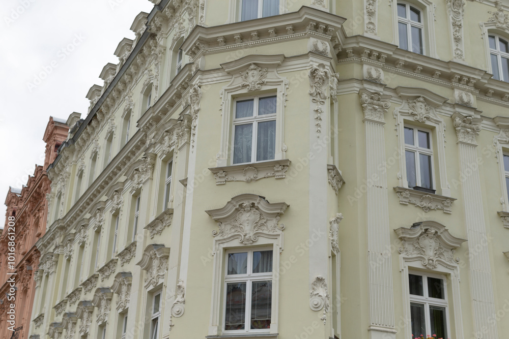 Fototapeta premium A large white building, featuring numerous windows, is situated prominently on the corner of the bustling street, catching the eye of passersby