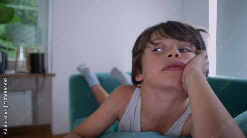 Young boy lying on couch, head propped on hand, eyes gazing upward, reflecting a moment of curiosity and daydreaming in a casual and cozy indoor environment Young boy lying on couch, head propped on hand, eyes gazing upward, reflecting a moment of curiosity and daydreaming in a casual and cozy indoor environment