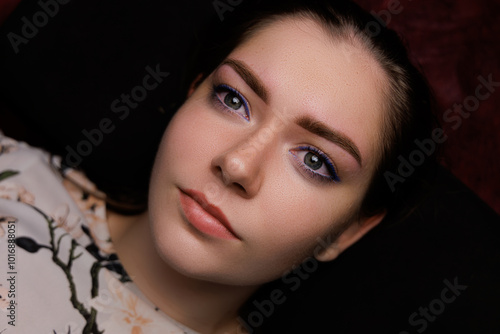 The young woman relaxes comfortably in a beauty studio, displaying her freshly tattooed eyebrows that enhance her facial features. The atmosphere is calm and inviting. photo