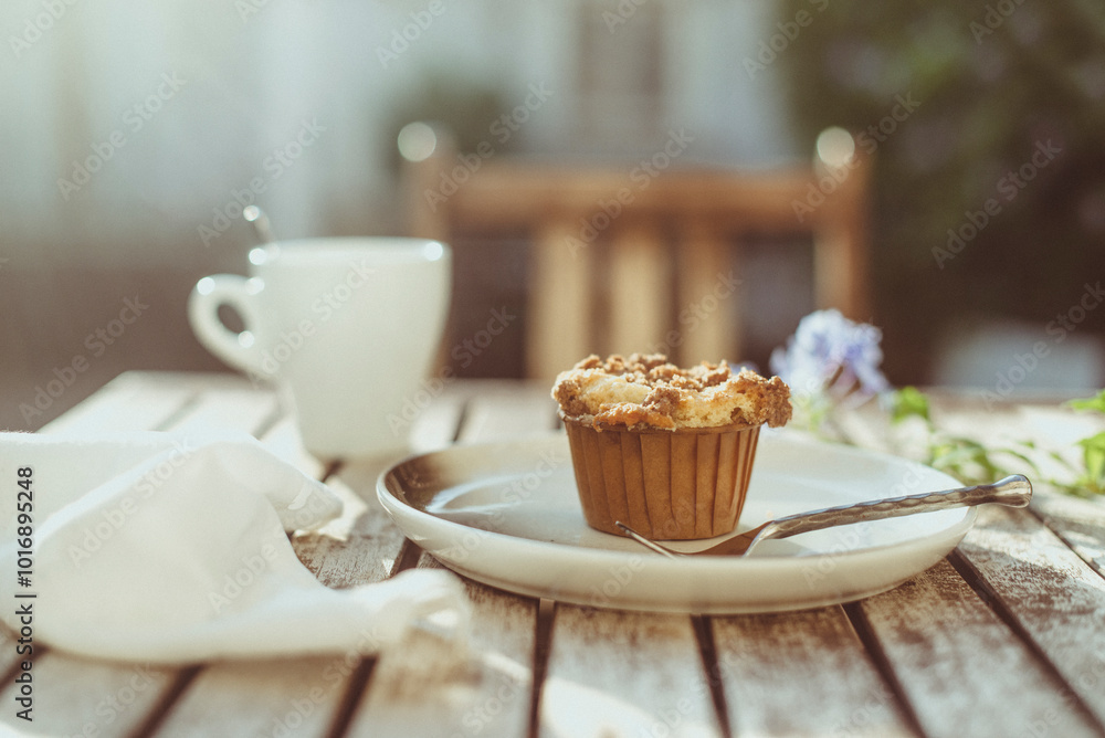 Close-up of a homemade crumble Cupcake and a cup of coffee on a garden table in sunlight Close-up of a homemade crumble Cupcake and a cup of coffee on a garden table in sunlight