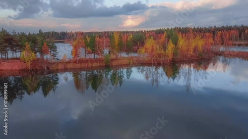 The autumn forest along the shore is reflected from the water surface.