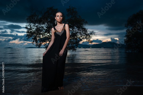 Beauty and nature. Fairy and sensual portrait of pretty young woman wearing long black dress against dramatic sky and sea view photo