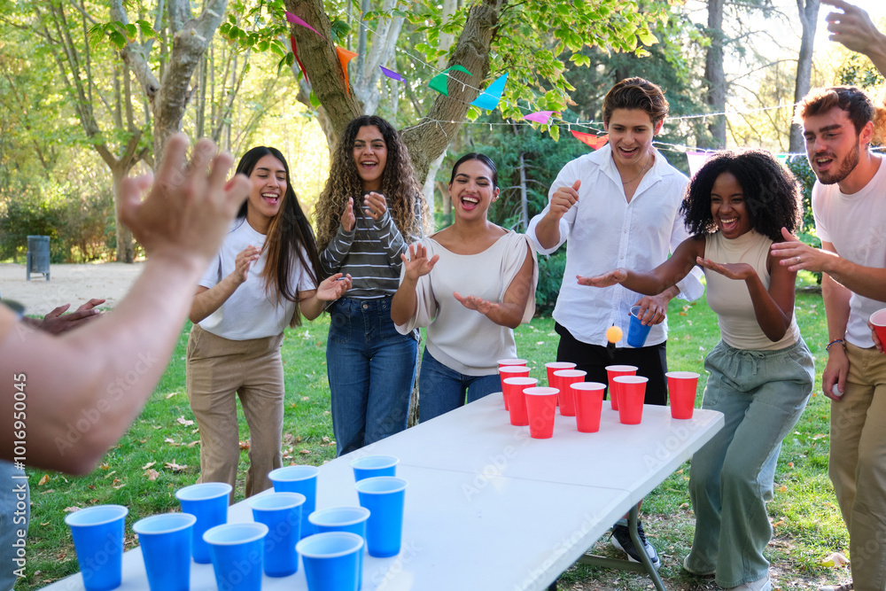 Cheerful young people playing beer pong in park on sunny day