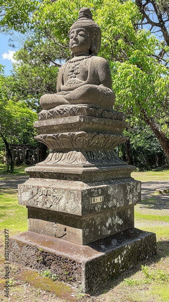 Fototapeta premium Ancient stone Buddha statue surrounded by lush greenery in a tranquil park setting