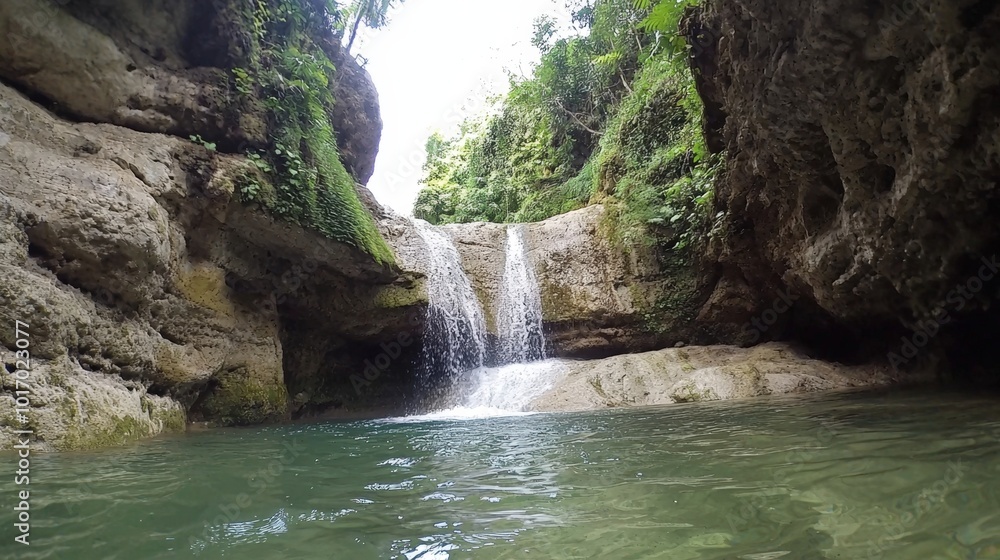 Naklejka premium Serene waterfall cascading into a tranquil pool surrounded by lush greenery in nature’s embrace