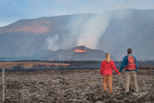 A hiking couple is observing the eruption of Sundhnúkagígar volcano in Iceland's Skógfellahraun lava field, August 2024. photo