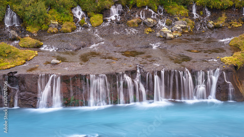 Hraunfossar waterfall cascading from lava rocks into the turquoise Hvítá River, surrounded by lush greenery. photo