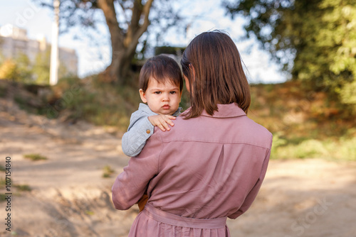 Portrait of happy loving mother hugging her baby son in the sunny park near river