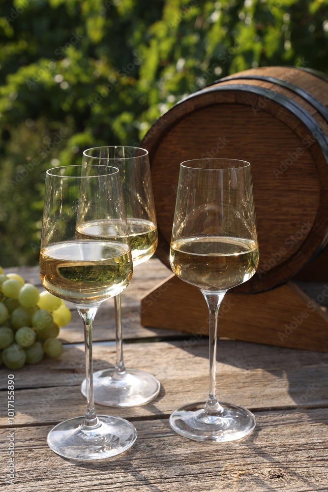Tasty wine in glasses, grapes and barrel on wooden table outdoors Tasty wine in glasses, grapes and barrel on wooden table outdoors