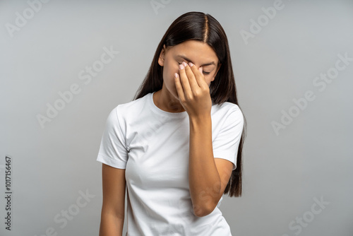 Photos Weary, emotionally drained teenage girl rubs tired eyes, slouched against isolated gray wall