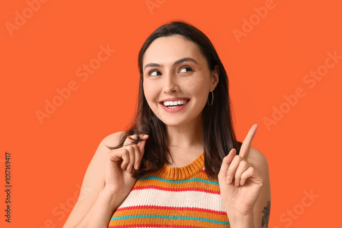 Smiling young woman pointing at something on orange background