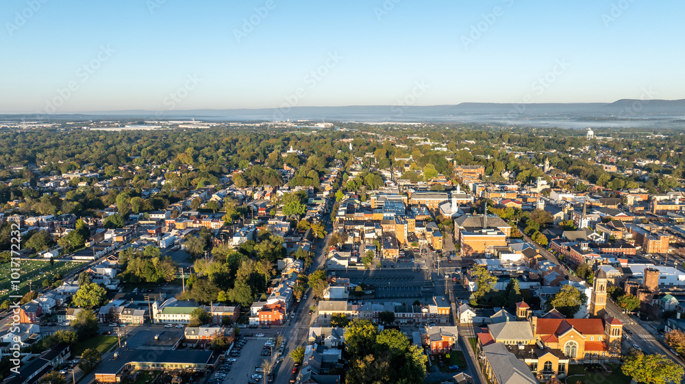 Obraz premium Aerial view of Carlisle, PA, showcasing a mix of residential, commercial buildings, and tree-lined streets under a clear morning sky.