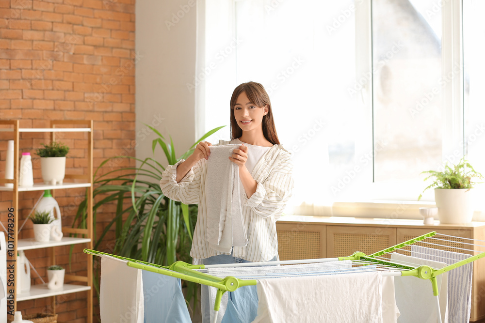 Young woman folding clean towel near dryer in laundry room Young woman folding clean towel near dryer in laundry room