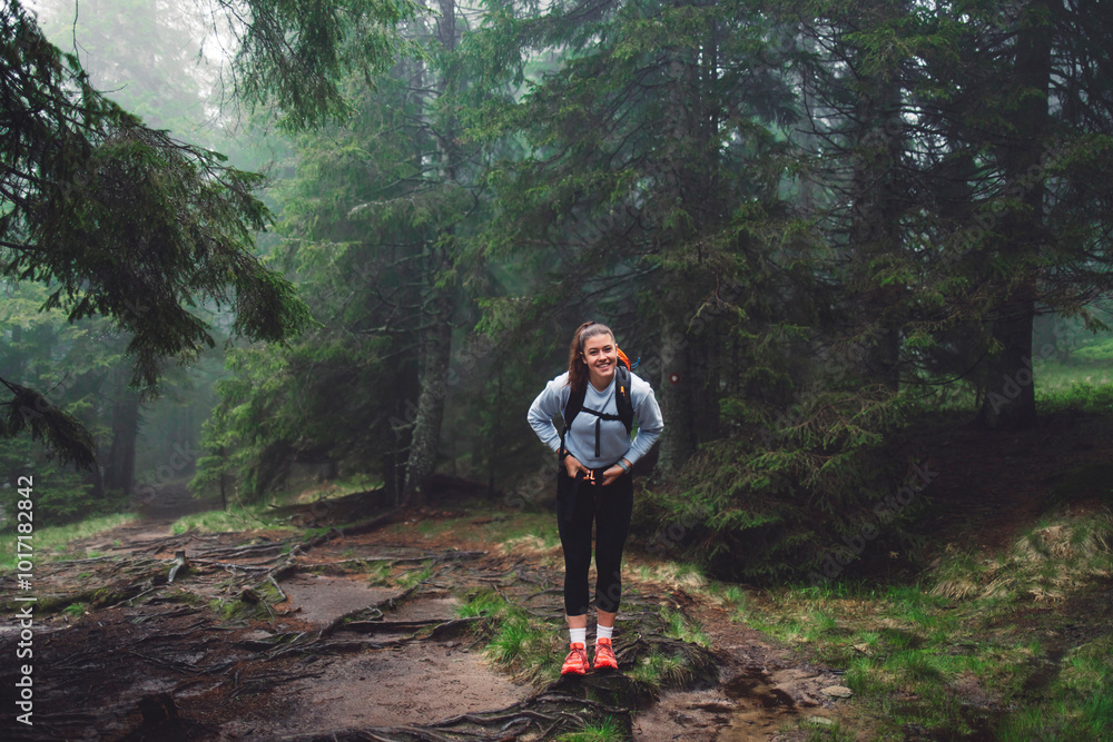 Obraz premium A person running through a misty forest, navigating over tree roots and muddy ground. The scene captures the essence of outdoor adventure and fitness, surrounded by lush greenery and fog.