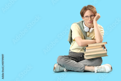 Upset male student with books sitting on blue background