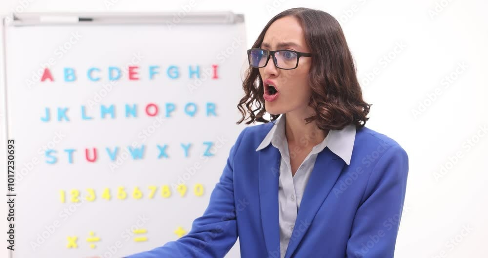 Angry teacher shouts pointing at textbook against whiteboard with English alphabet. Woman in eyeglasses expresses dissatisfaction with students mistakes Angry teacher shouts pointing at textbook against whiteboard with English alphabet. Woman in eyeglasses expresses dissatisfaction with students mistakes