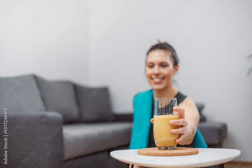 A young woman drinks a vegetable and fruit smoothie in her living room and doing yoga on yoga mat. A young woman drinks a vegetable and fruit smoothie in her living room and doing yoga on yoga mat.
