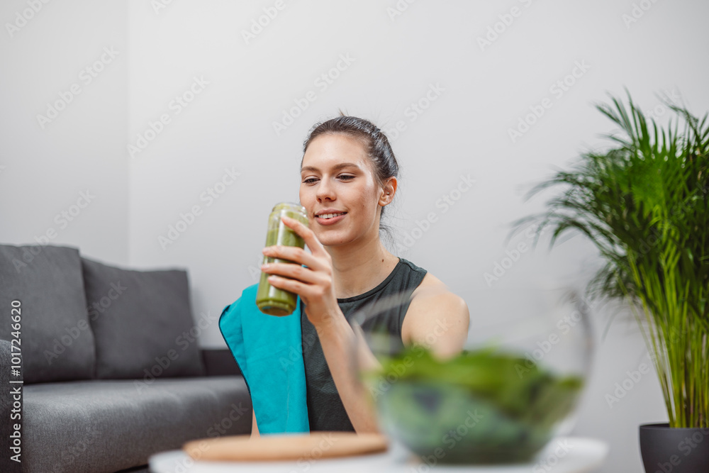A young woman drinks a vegetable and fruit smoothie in her living room and doing yoga on yoga mat. A young woman drinks a vegetable and fruit smoothie in her living room and doing yoga on yoga mat.