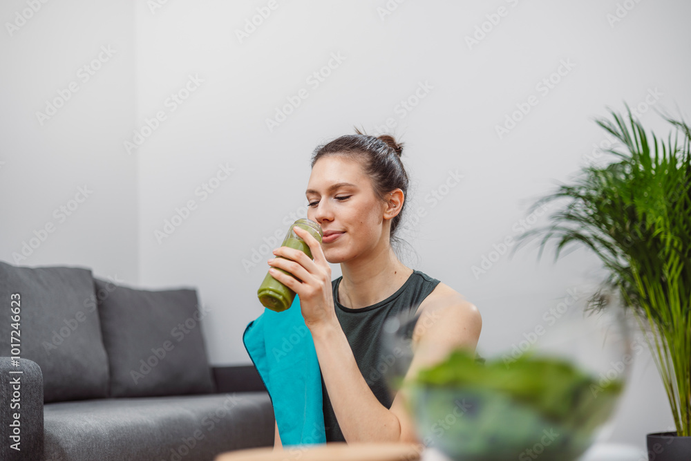 A young woman drinks a vegetable and fruit smoothie in her living room and doing yoga on yoga mat. A young woman drinks a vegetable and fruit smoothie in her living room and doing yoga on yoga mat.
