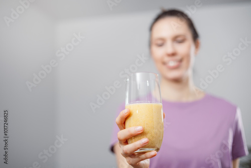 A young woman drinks a vegetable and fruit smoothie in her living room and doing yoga on yoga mat.