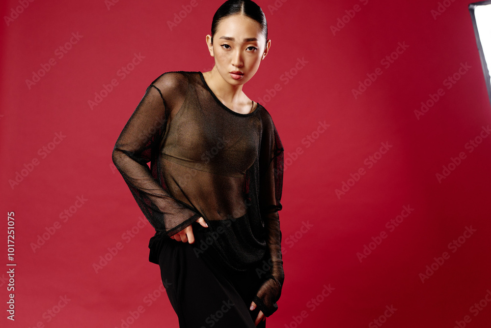 Φωτογραφία Asian woman in sheer top and black skirt posing in front of red background with