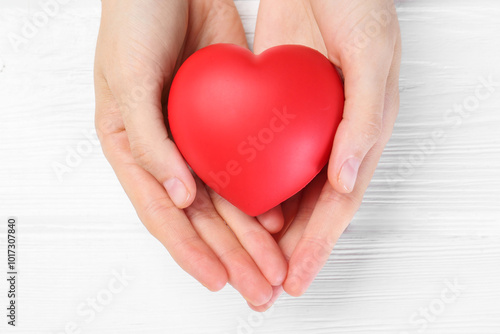 Woman holding red heart on white wooden background, top view